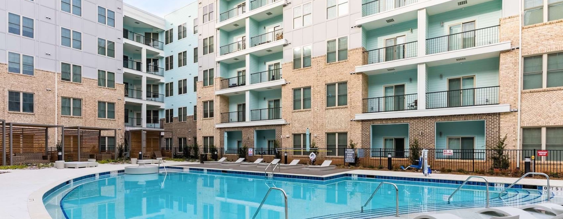 Urban Apartments for Rent in University City, NC - Mason - Outdoor Courtyard with Pool, Spacious Sun Deck, Submerged and Poolside Lounge Chairs, and View of Apartment Building.